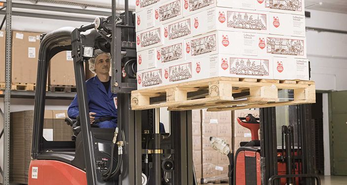 Mitarbeiter mit Stapler verfährt eine Palette verpackter Lebkuchen