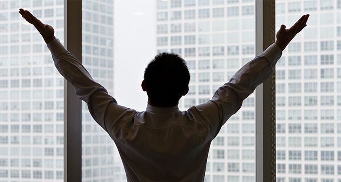 Eine Person steht in einem Hochhaus am Fenster und streckt beide Arme nach oben