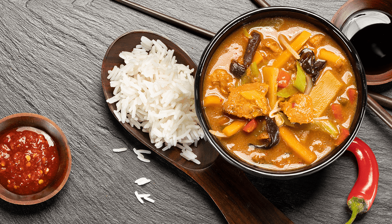 Feritggericht: Hähnchen in pikanter Soße mit Reis auf einem schwarzen Holztisch